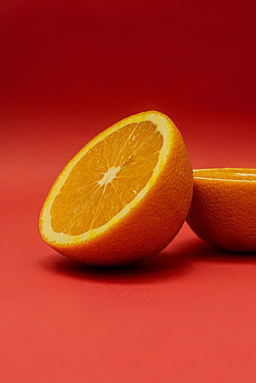 A sliced orange on a red background, with one half facing forward and the other half partially visible behind.