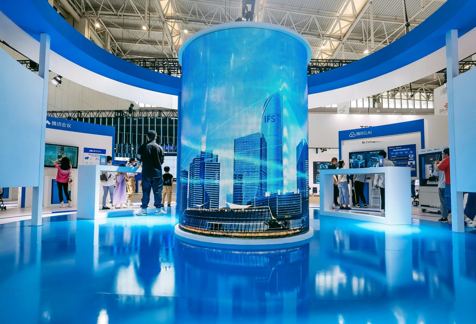 Technology exhibit at a convention with a large digital cityscape display, various booths, and people interacting with tech displays.