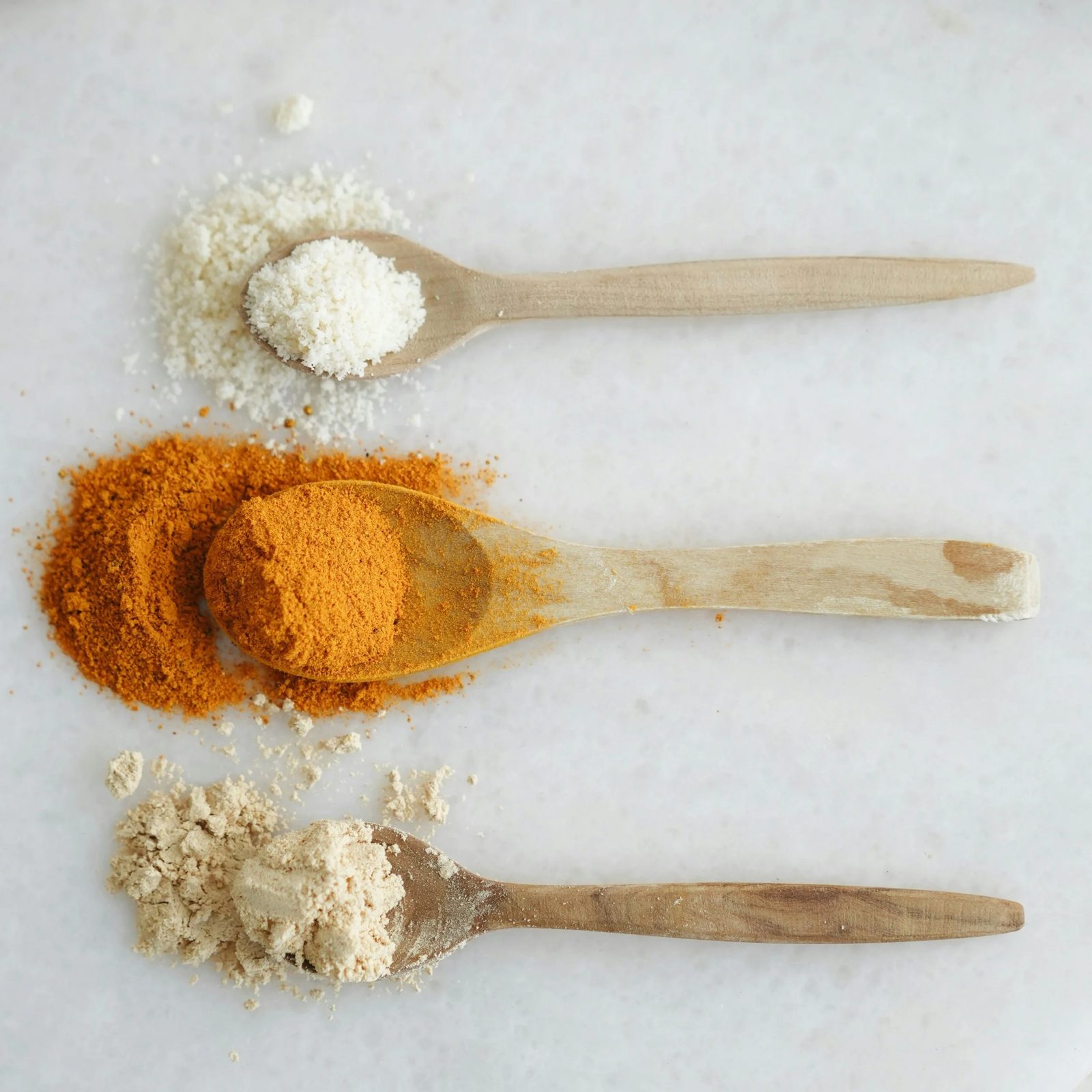 Three wooden spoons containing different powdered spices arranged on a white surface